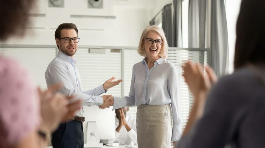 Boss congratulating older worker in front of colleagues