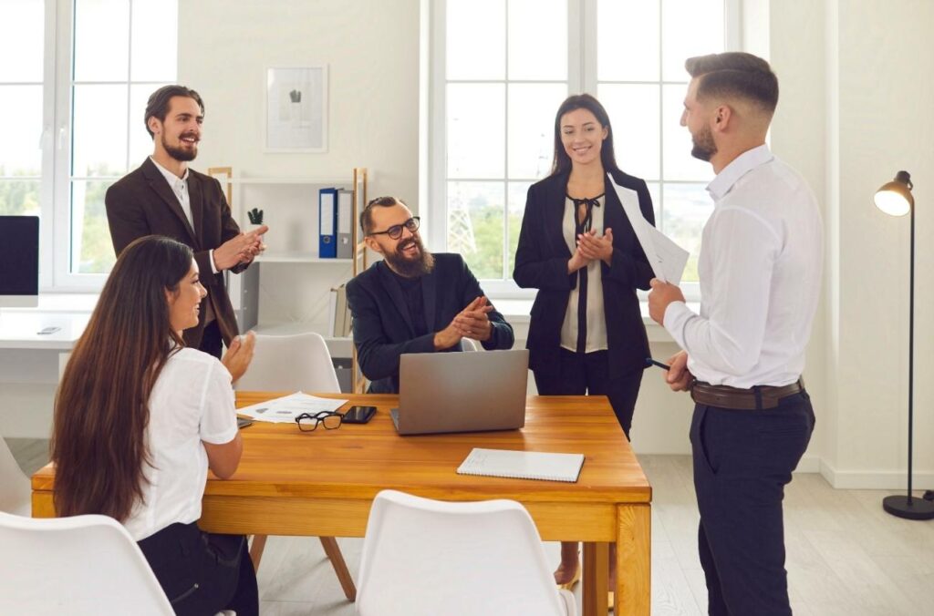 Boss praising employee for a job well done in front of other people by clapping for him.