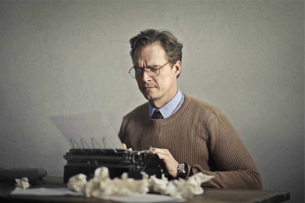 Man at typewriter with wadded up papers around him because he's making mistakes at work